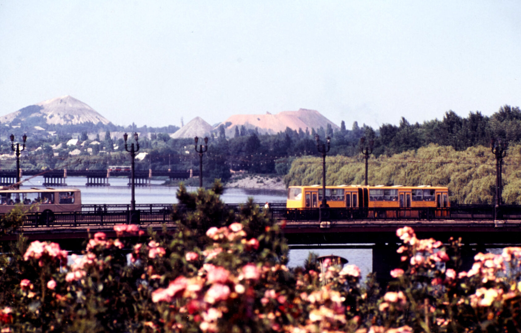 DX677/3/1 Donetsk, view over river showing rose bushes in foreground, trolley bus and trams crossing river bridges and spoil heaps in background
